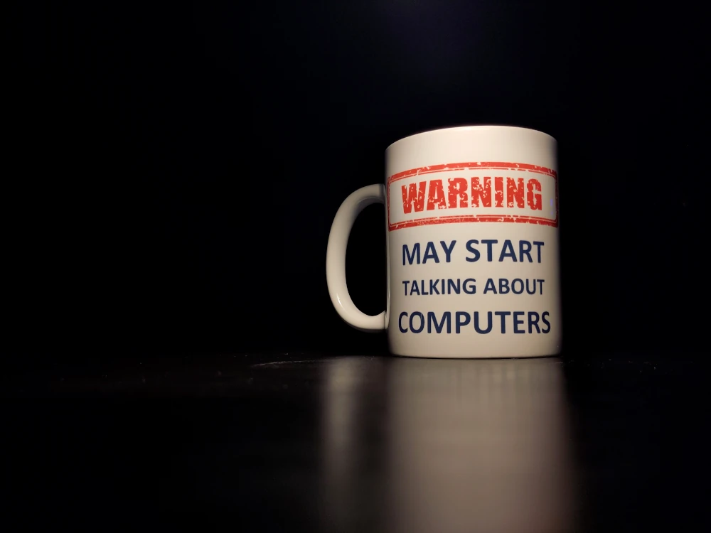Image of a white drink mug against a black background with the text “Warning: may start talking about computers” written on it